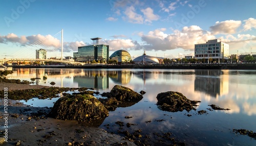 A tranquil cityscape reflected in the calm waters of a river, showcasing modern architecture and a serene coastal setting at dawn.