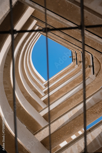 A mesmerizing upward shot of modern architectural curves framed through vertical steel bars, blending geometric elegance with clear blue skies.