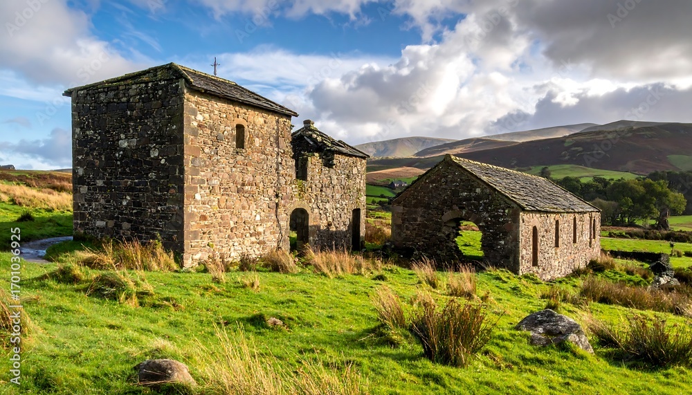 Fototapeta premium Two weathered stone buildings stand on a grassy hill, overlooking a valley with rolling hills and distant mountains.