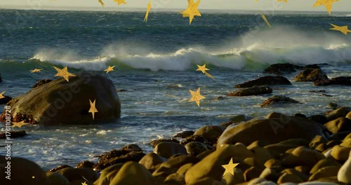 Obraz Ocean waves rolling and breaking on rocky shoreline, with round boulders and golden star sparkles