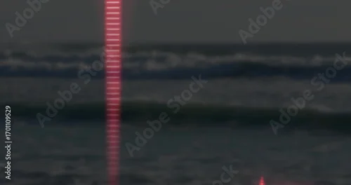 Obraz Shining narrow vertical red beam reflecting off ocean waves at seaside at night, faint horizon line