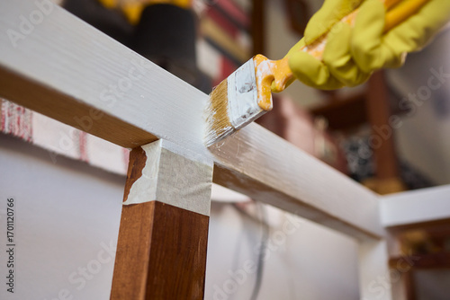 Engage in DIY chair restoration using a paint brush and protective gloves for the process