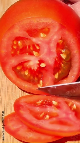 Close-up of ripe tomato cut into round slices with kitchen knife on wooden cutting board, showing smooth knife motion and fresh texture of juicy vegetable during preparation. asmr