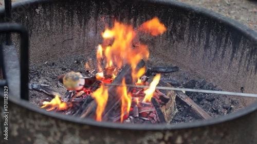 Warm fire lights comes from soft burning camp fire in metal fire ring at camp site, in nature
