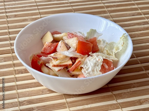 Salad of fresh vegetables as tomatoes, onions, apples, Chinese cabbage in a white plate on bamboo background