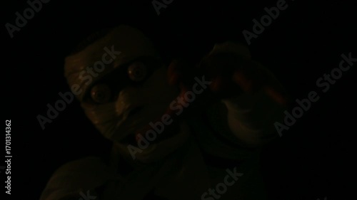 Dark scene of creepy mummy figure wrapped in bandages with a haunting expression under moody, dark lighting.