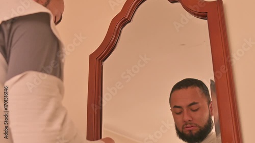 Man in creepy mummy wrapped custom with bandages trying some Halloween masks Infront of mirror at home.
