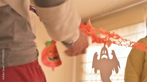 A close-up of woman with painted face holding vibrant Halloween-themed paper decorations, featuring ghost designs in bright colors, reflecting the festive spirit and creativity of the holiday season.