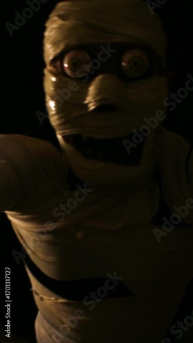 Vertical video of creepy mummy figure wrapped in bandages with a haunting expression under moody, dark lighting.