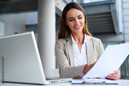Professional woman reviewing documents near laptop business