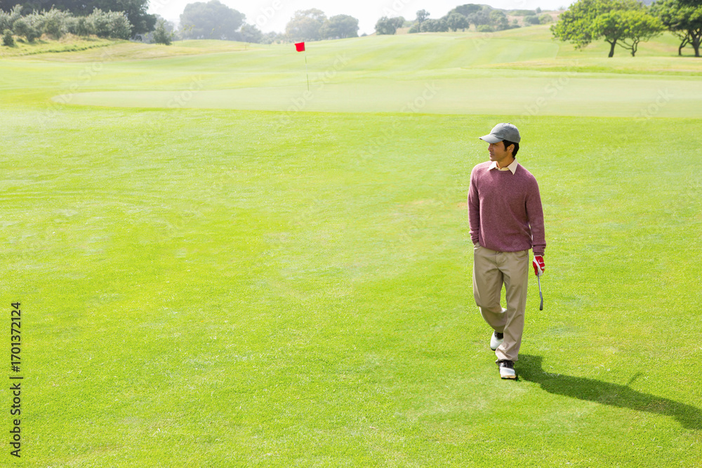 Obraz premium Golfer walking across vibrant green fairway toward red flag, holding putter with red glove