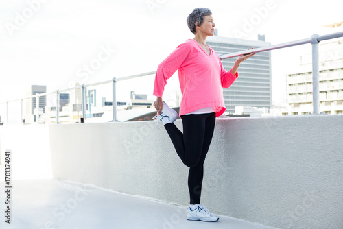 Obraz na plátne Woman performing standing quadriceps stretch on rooftop terrace overlooking city