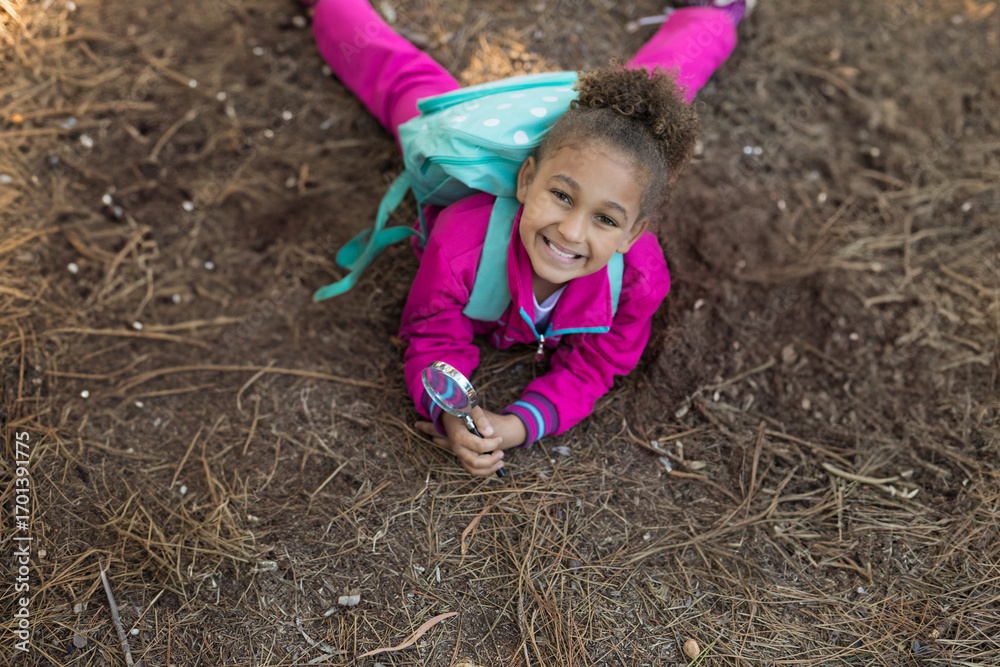 Fototapeta premium Exploring forest floor, child in pink outfit using magnifying glass, smiling happily, copy space