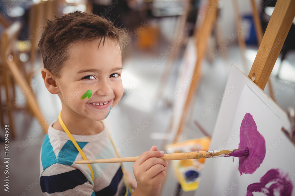 Naklejka premium Smiling boy painting on easel in school art class, enjoying creativity
