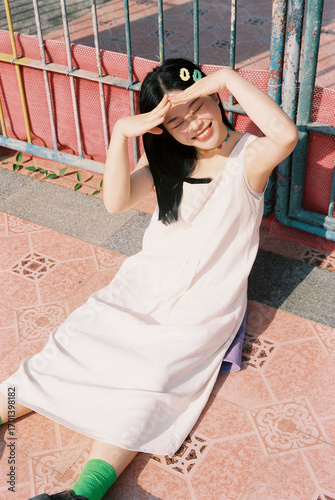 A smiling young woman in a white dress sitting outdoors, enjoying the sun and warmth.