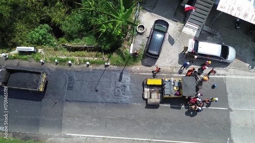 Aerial view of asphalt road repair with trial compaction process, testing surface quality before final paving. Infrastructure construction footage