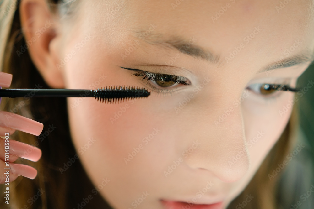 Obraz premium A beautiful teenage girl applying mascara to her eyelashes in a close-up shot. Self-applied makeup highlighting youthful style and confident grooming.