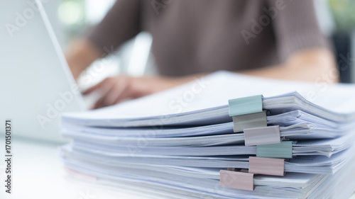 Business woman working on laptop computer with stack of paper document for searching and checking document on folder paper at busy work on desk office, close up