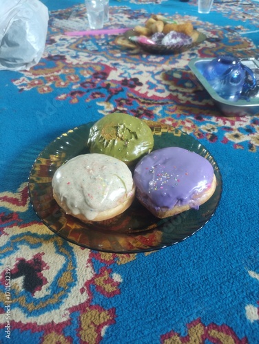 Three donuts on a plate placed on a blue carpet, sweet food with colorful decoration