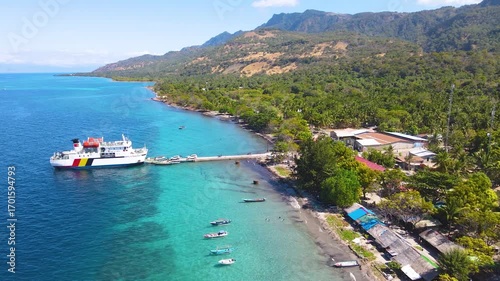 A beautiful aerial view of a ferry docked at the port of Atauro Island, Timor-Leste. The ship waits for passengers over the stunningly clear turquoise water with the island's mountains behind