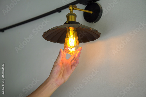 Tableau sur toile Illuminating Brilliance: A hand reaches towards a warm, glowing lightbulb, a testament to innovation, technology, and human ingenuity