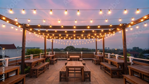 rooftop dining Rooftop dining area with wooden seating and string lights against a sunset backdrop.
