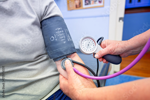 Nurse checking blood pressure BP of female patient, GP general practice Australia, medical healthcare clinic