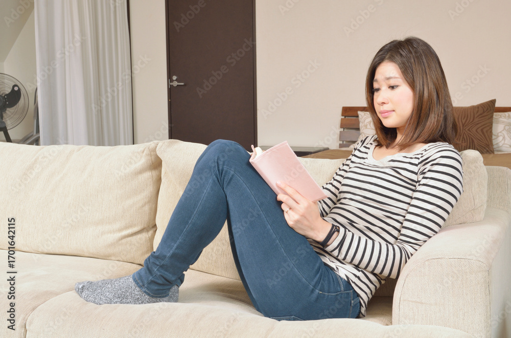 Fototapeta premium リビングルームで読書する若い女性