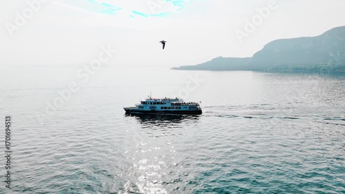Ferry departing from a lakeside town on Lake Garda, aerial drone shot. Public transport network linking multiple ports around the lake