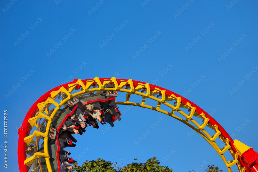 Fototapeta premium Riders experience an exhilarating upside-down inversion on a vibrant red and yellow roller coaster