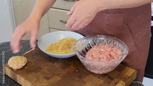 Cooking cutlets. A girl in a home kitchen shapes minced meat into a shape with her hands. A cook rolls minced meat cutlets in breadcrumbs