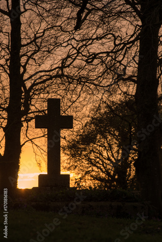 Ancient cross tombstone silhouetted at sunset