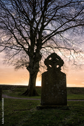 Ancient Celtic cross tombstone silhouetted at sunset
