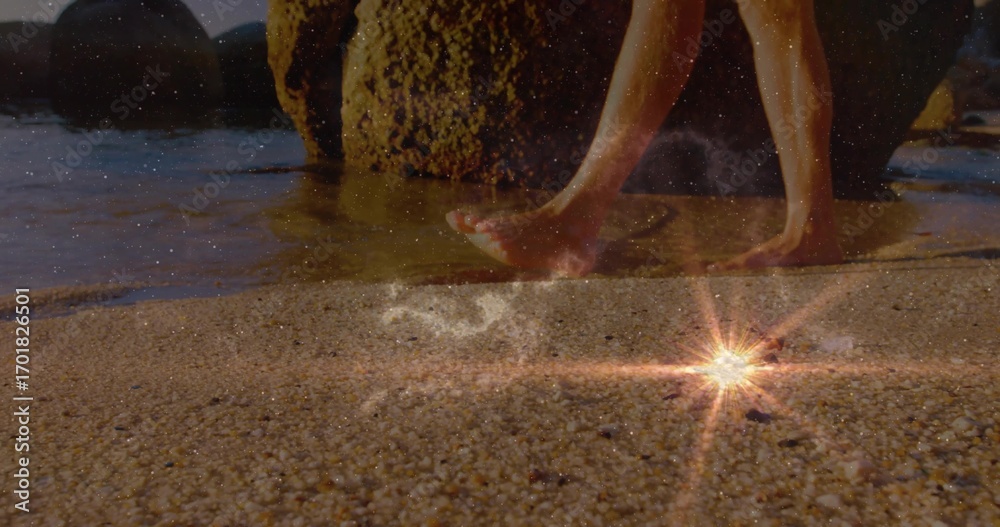 Naklejka premium Stepping bare feet on wet pebbly shoreline by mossy rocks with starburst reflection, copy space