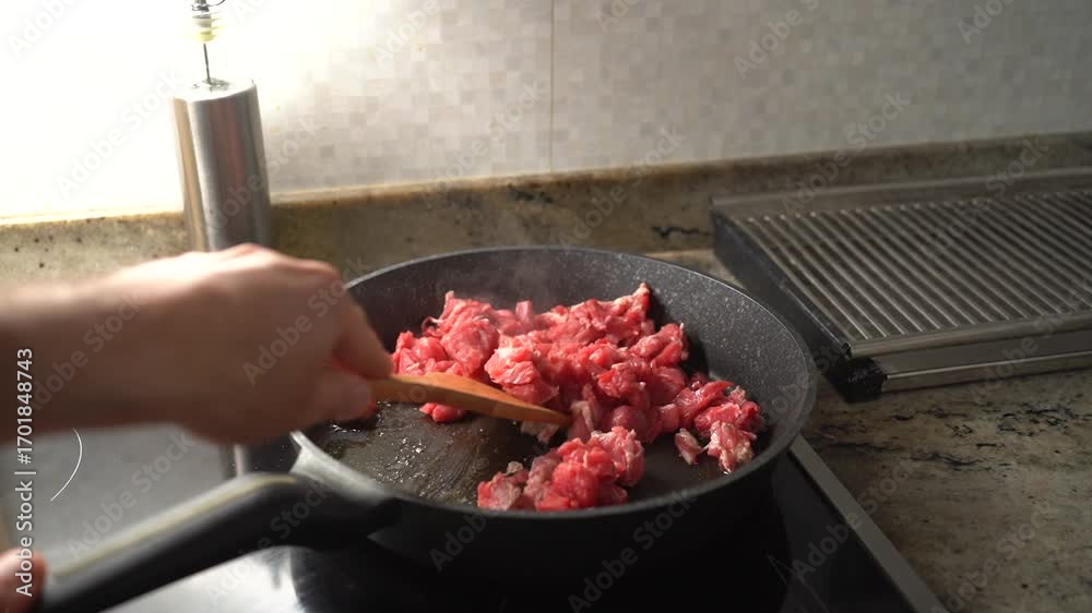 custom made wallpaper toronto digitalClose-up of raw beef cubes being fried in a pan with a wooden spatula, cooking process in a home kitchen.