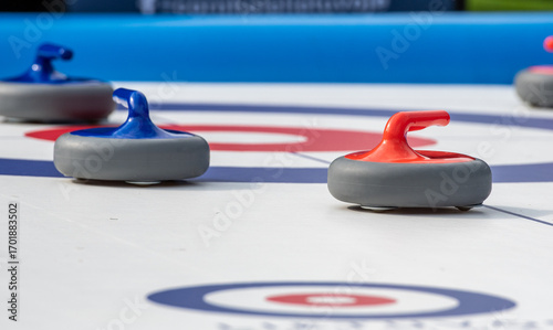 Tableau sur toile Several curling stones with red and blue handles are positioned on a recreational curling sheet