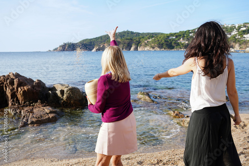 Mother and daughter scattering ashes at the seaside