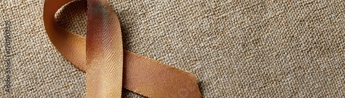 A close-up of a golden ribbon on a textured beige background, symbolizing awareness and support for various causes, Ideal for campaigns, fundraising, or educational materials about health issues,
