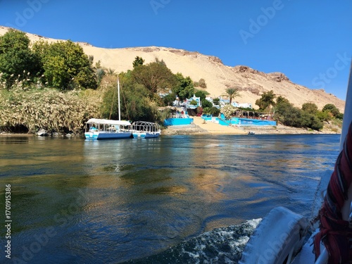 Colorful Nubian House on the Nile River, A vibrant view of a brightly painted house on the sandy banks of the Nile River. The building, a typical example of Nubian architecture.