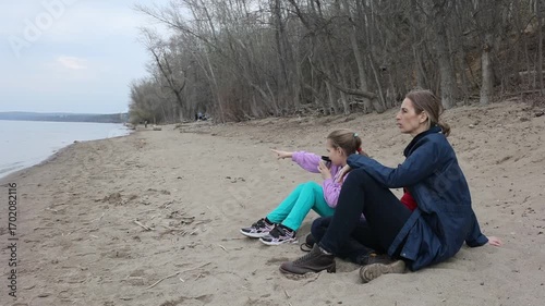 family mom and daughter is eight years old drinking tea and eating sandwiches sitting on the sand near the river on a spring day.  Family leisure with kids at spring.