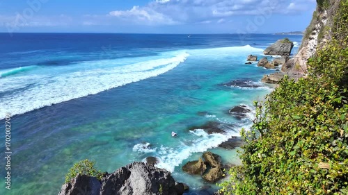 Tranquil seascape showcasing rugged cliffs and gentle surf, waves softly crashing against rocks, embodying Bali, Indonesia enchanting landscape in stunning slow motion