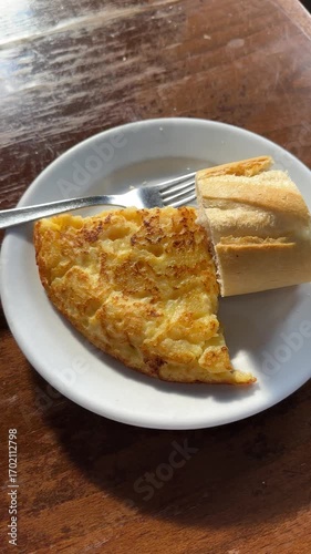 Close-up of a classic Spanish omelette with potato, paired with crusty bread on a white plate, perfect representation of Spanish tapas culture and comfort food.