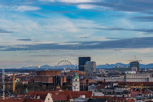 Blick über München auf das Riesenrad im Werksviertel und die schneebedeckten Alpen bei Sonnenuntergang