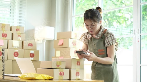 Young Asian female entrepreneur manages online business orders from home using smartphone, laptop and e-commerce work package.