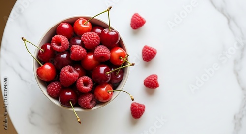Fresh red cherries and raspberries in a bowl on a white marble background top view.