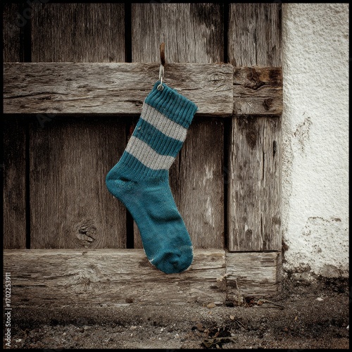 Worn striped wool sock hanging on weathered wooden fence with textured background