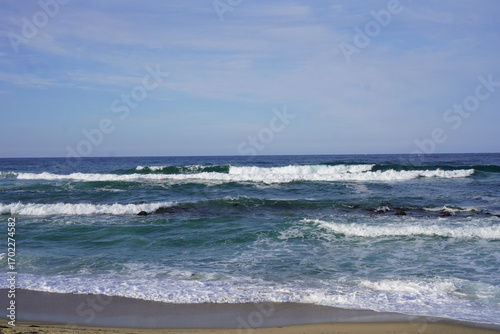 Scenic ocean waves rolling onto sandy beach with clear blue sky, peaceful seascape landscape background, relaxing coastal view of sea horizon and surf water