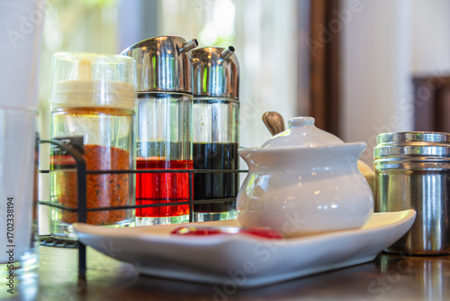 Asian condiment set on restaurant table, including fish sauce, chili vinegar, soy sauce, sugar jar, and chili powder, traditional seasoning for noodles and Asian cuisine.