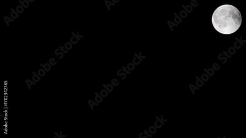 A time-lapse shot of a bright full moon, shadowed by an eclipse, shining in the night sky over a dark landscape, creating an atmosphere of calm and tranquility.