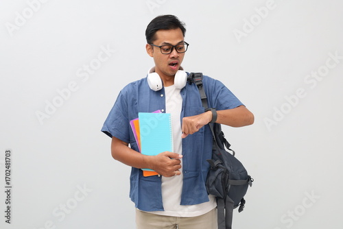Young asian college student wearing casual clothes, glasses, backpack, holding books, looking at watch on hand with shocked expression, late for school concept, isolated on white background.